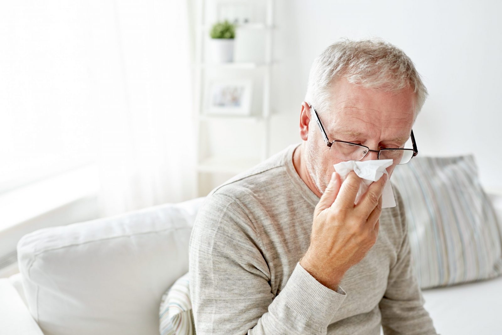 man with glasses blowing nose with tissue